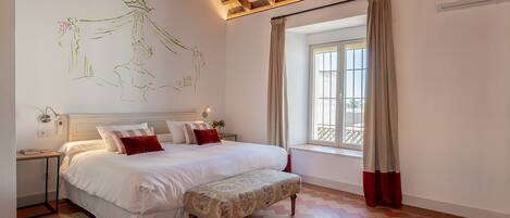 Un dormitorio con cama, mesitas de noche, una ventana con cortinas y una pared con mural.