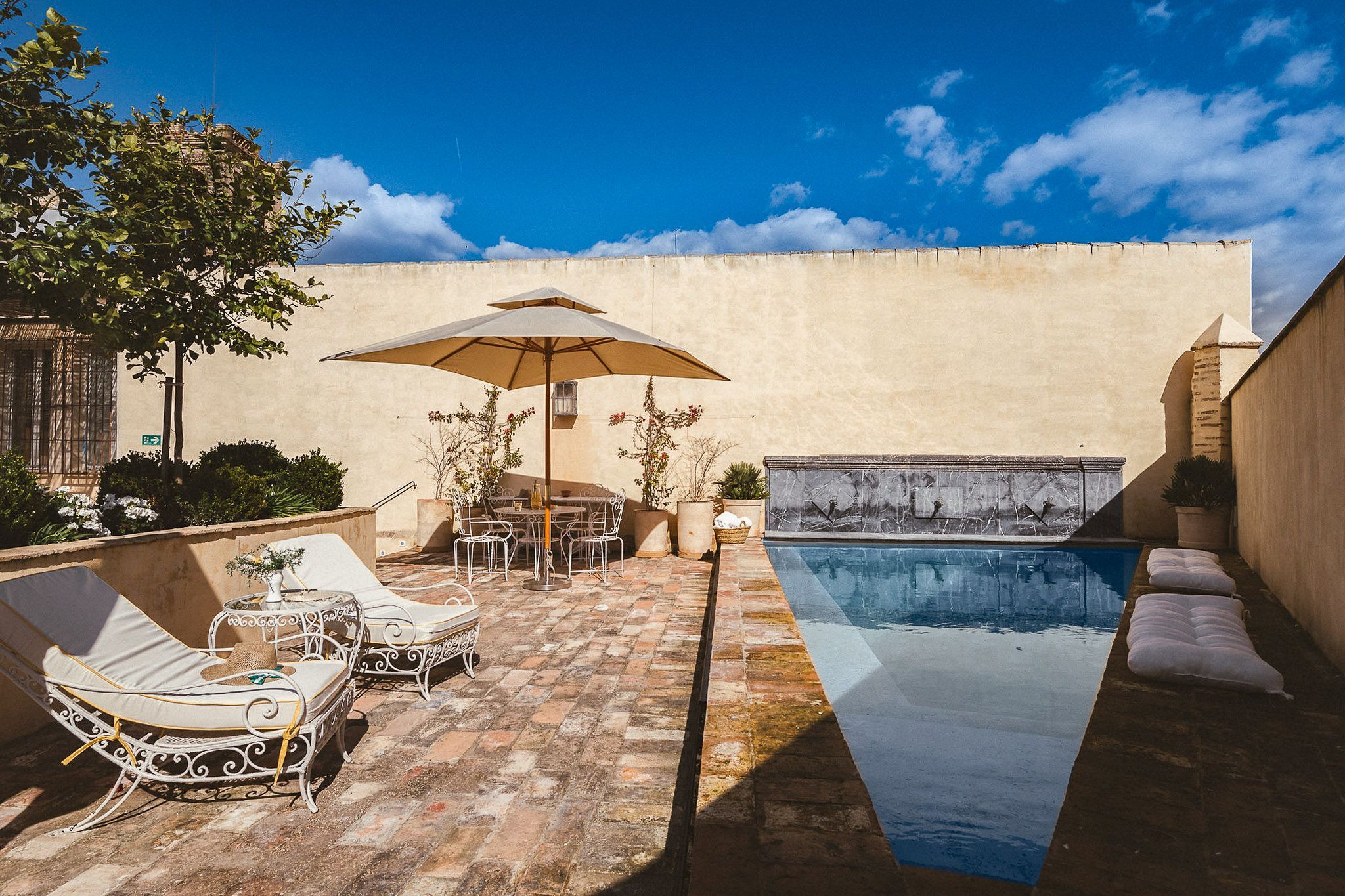 Zona junto a la piscina con sillones de descanso, una mesa y una sombrilla.