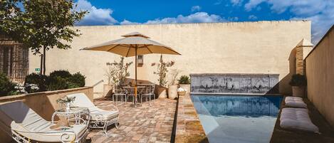 Zona junto a la piscina con sillones de descanso, una mesa y una sombrilla.