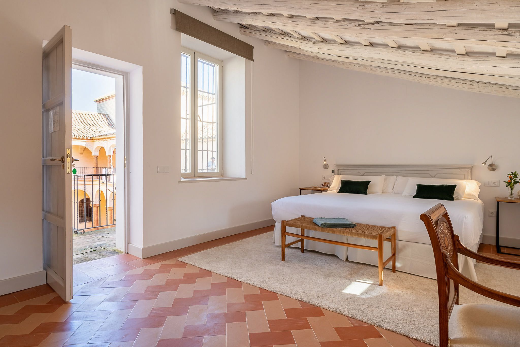 Quarto com cama, um banco, uma janela e vista para área externa.