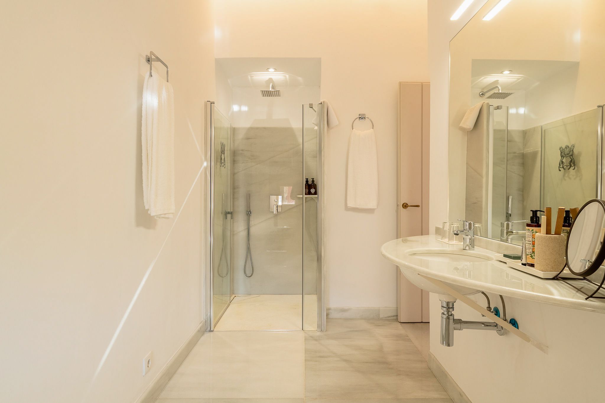 Een moderne badkamer met een douchecabine van glas, een grote spiegel en een wastafel met toiletartikelen.