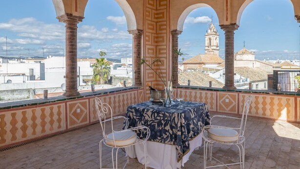 A terrace with a table and chairs, overlooking a cityscape with buildings and a tower.