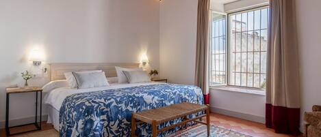 A bedroom with a bed, bedside tables, a bench, a window with curtains, and a patterned rug.