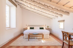 A bedroom with a bed, bedside tables, a bench, a chair, a window, and a ceiling with exposed beams. - Palacio Catalina - Ten Bedroom Villa, Sleeps 22 (Lora del Río)