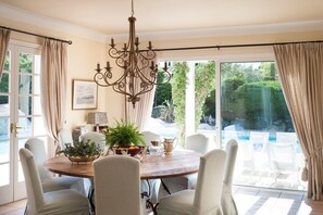 Uma sala de jantar com uma mesa redonda, cadeiras, um candelabro e vista para uma piscina.