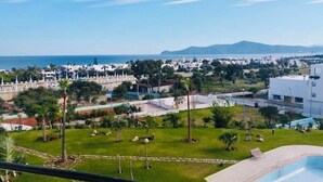 A residential area with a pool, greenery, and a view of the sea and distant mountains. - Superb Colina Smir apartment, swimming pool view in front of magnificent Kabila Beach (Marina Smir)