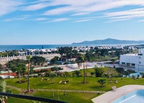 A residential area with a pool, greenery, and a view of the sea and distant mountains. - Superb Colina Smir apartment, swimming pool view in front of magnificent Kabila Beach (Marina Smir)