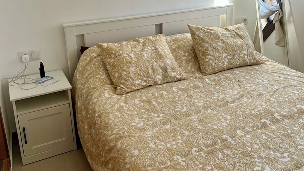 A neatly made bed with a patterned bedspread, a bedside table with a lamp, and a mirror on the wall. - Superb Colina Smir apartment, swimming pool view in front of magnificent Kabila Beach (Marina Smir)