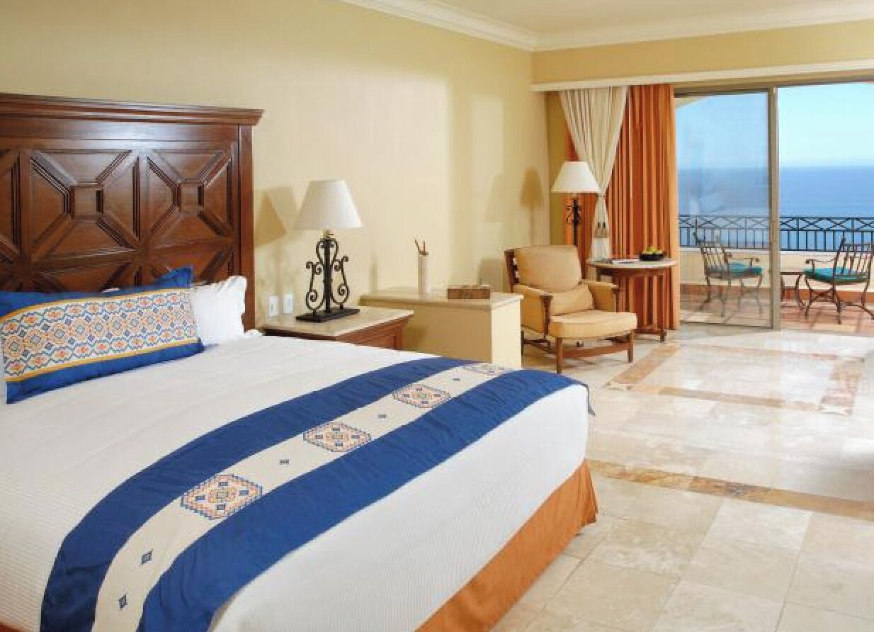 Une chambre d’hôtel avec un grand lit, une chaise, une petite table et un balcon donnant sur l’océan.