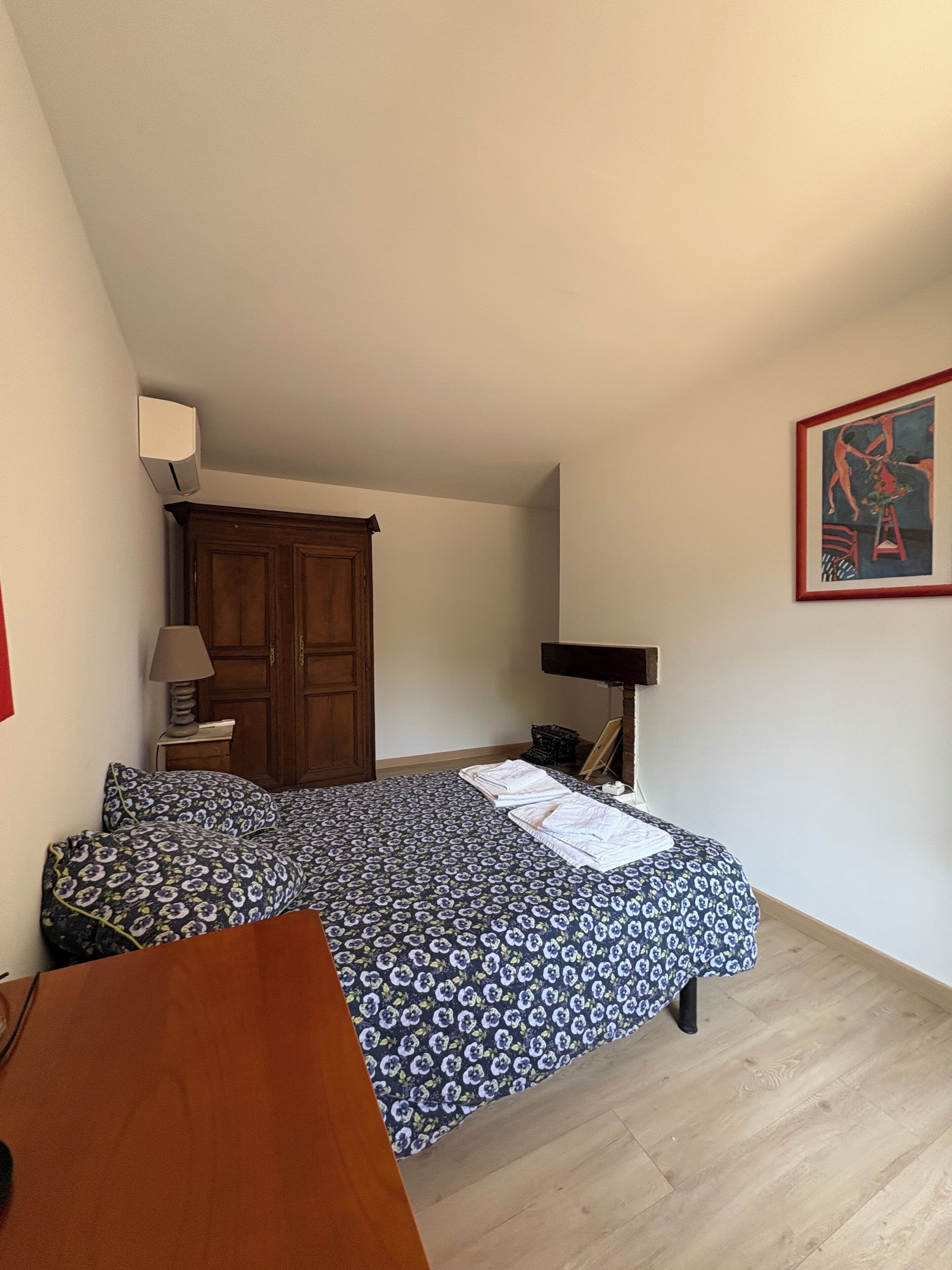 Ein Schlafzimmer mit einem Bett, einem Holzschrank, einem Schreibtisch und einem gerahmten Bild an der Wand.