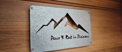 Una placa de metal con un diseño de montaña y el texto 'Peace & Rest in Pirineum' sobre una superficie de madera.