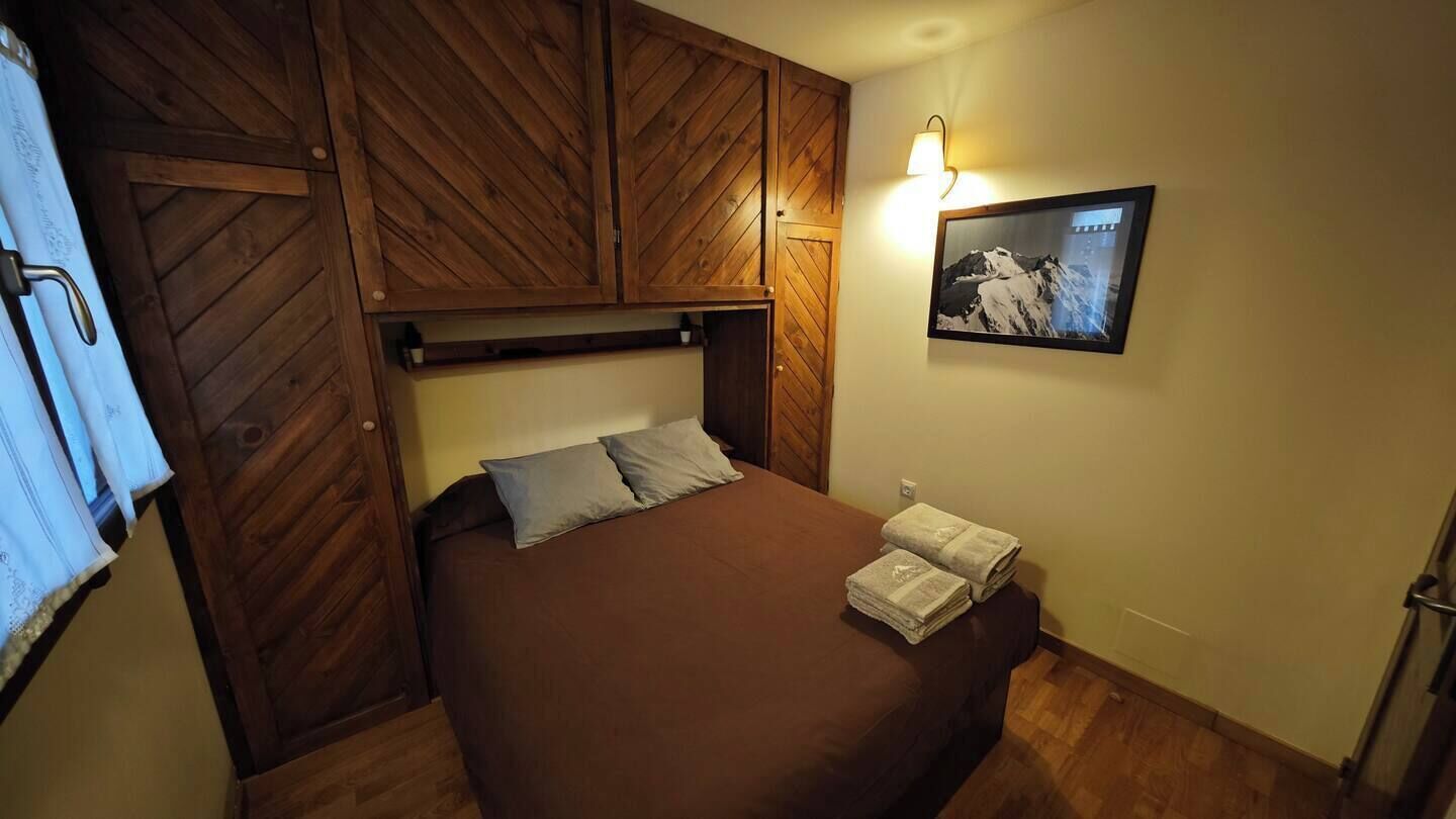 Une chambre à coucher avec une tête de lit en bois, un lit avec une literie marron, une lampe fixée au mur et un tableau représentant une montagne.