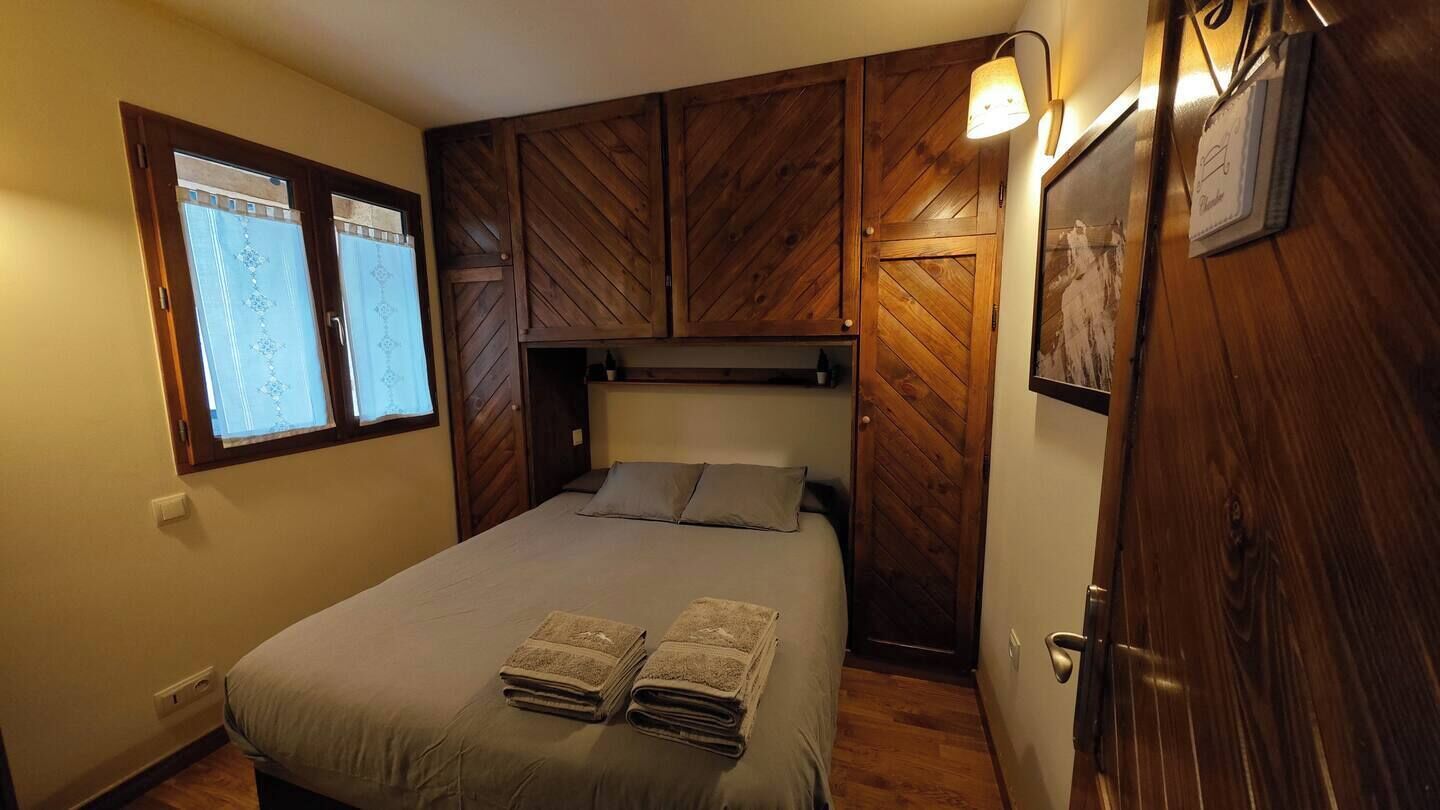 Quarto com cama, painéis de madeira, janela com persianas e porta com moldura de quadro.