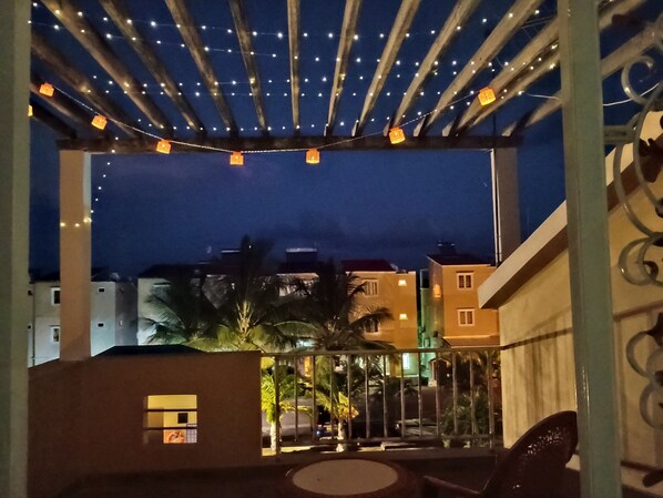 A balcony with string lights, a small table, and chairs.