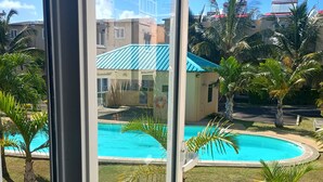 On aperçoit clairement une piscine entourée de palmiers et un bâtiment surmonté d’un toit bleu.