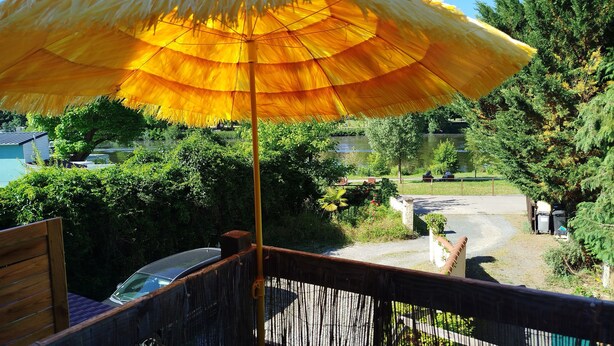 Una terraza de madera con una sombrilla amarilla, un coche y vistas a un lago y árboles.