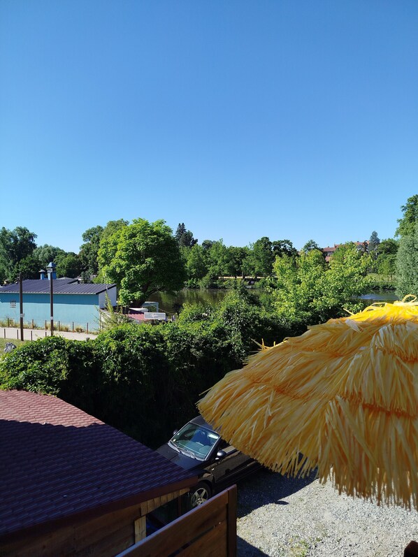 A beach umbrella, a wooden deck, and a view of a lake with buildings in the background.