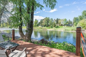 A deck with a view of a lake, surrounded by trees and a grassy area. - New Riverfront Home on 1 Acre - WiFi, Covered Deck (Grants Pass)