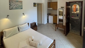 A hotel room with a bed, a small bedside table, a nightstand, a bathroom with a sink and mirror, and a kitchen area. - Delfinia Studios (South Pelion)