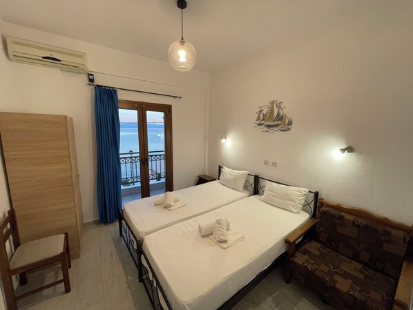 A hotel room with two beds, a wooden wardrobe, a balcony with a view, and a decorative wall piece. - Delfinia Studios (South Pelion)