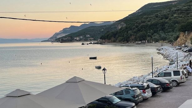 A seaside café with outdoor seating, a view of the sea, and parked cars along the beach. - Delfinia Studios (South Pelion)