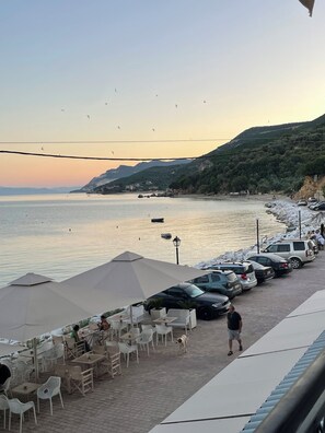 A seaside café with outdoor seating, a view of the sea, and parked cars along the beach. - Delfinia Studios (South Pelion)