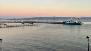 A harbor with a fishing boat docked, calm water, and distant mountains. - Delfinia Studios (South Pelion)