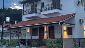 A two-story building with a tiled roof, balconies with metal railings, and a paved entrance area with potted plants. - Delfinia Studios (South Pelion)