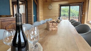 Una mesa de comedor de madera con una botella de vino y copas, una cesta tejida y vistas del exterior a través de ventanas amplias.