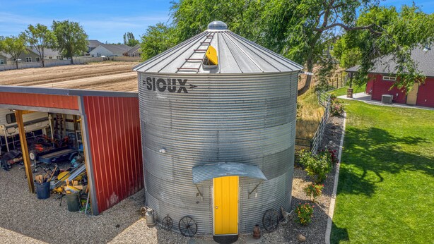 A large metal silo with a yellow door and a ladder on top, surrounded by gravel and a small garden.