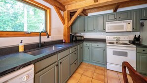A kitchen with green cabinets, a white stove, a microwave, and a sink.