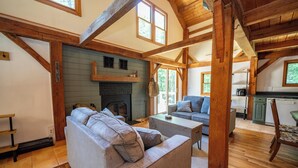 A cozy living room with a fireplace, wooden beams, a sofa, and a dining area.