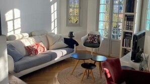 A living room with a sofa, a small round table, a red chair, and a bookshelf. - Charming 1920s house in Nice district (Nice)