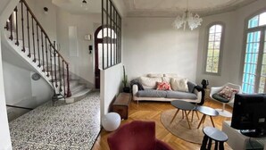 A spacious living room with a staircase, a sofa set, a television, and a chandelier. - Charming 1920s house in Nice district (Nice)