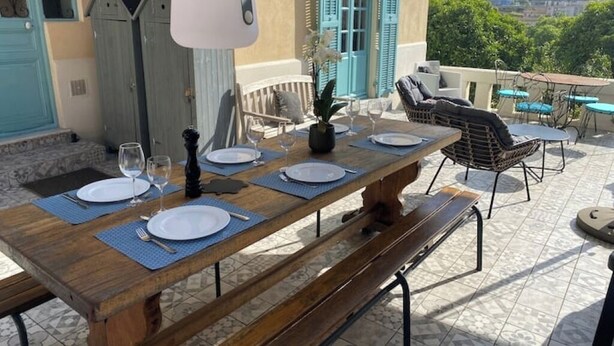 A wooden dining table set with plates, cutlery, and wine glasses, with a view of a cityscape in the background. - Charming 1920s house in Nice district (Nice)