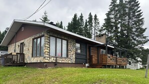 Eine rustikale Holzhütte mit Steinverkleidung, großen Fenstern und einer Holzterrasse.