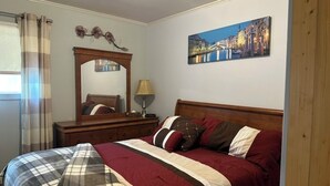 Ein Schlafzimmer mit einem Bett, einer Holzkommode, einem Spiegel, einer Lampe und einem Stadtbild an der Wand.