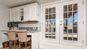 Una cocina con armarios blancos, un taburete de bar y una puerta doble con paneles de vidrio.