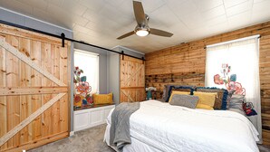 Un dormitorio con cama, paredes de madera, ventilador de techo y ventana con cortinas.
