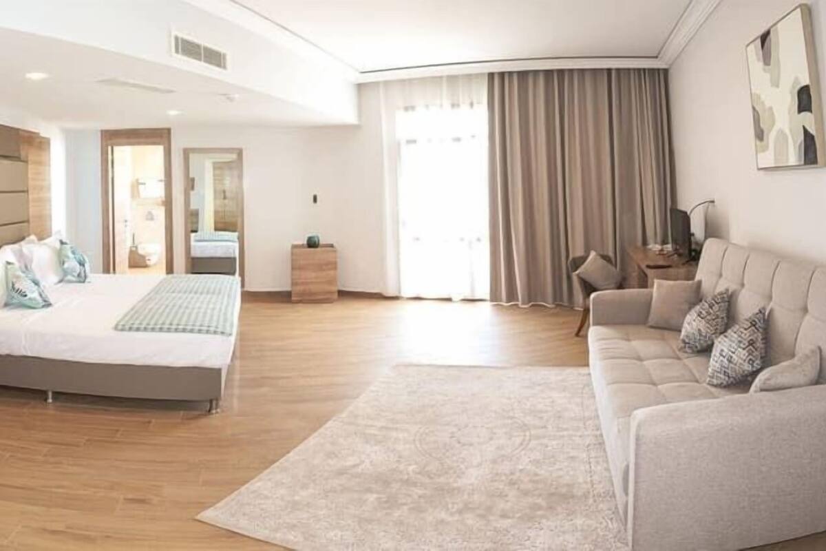 A modern bedroom with a large bed, a sitting area with a sofa, and a view of the outdoors.