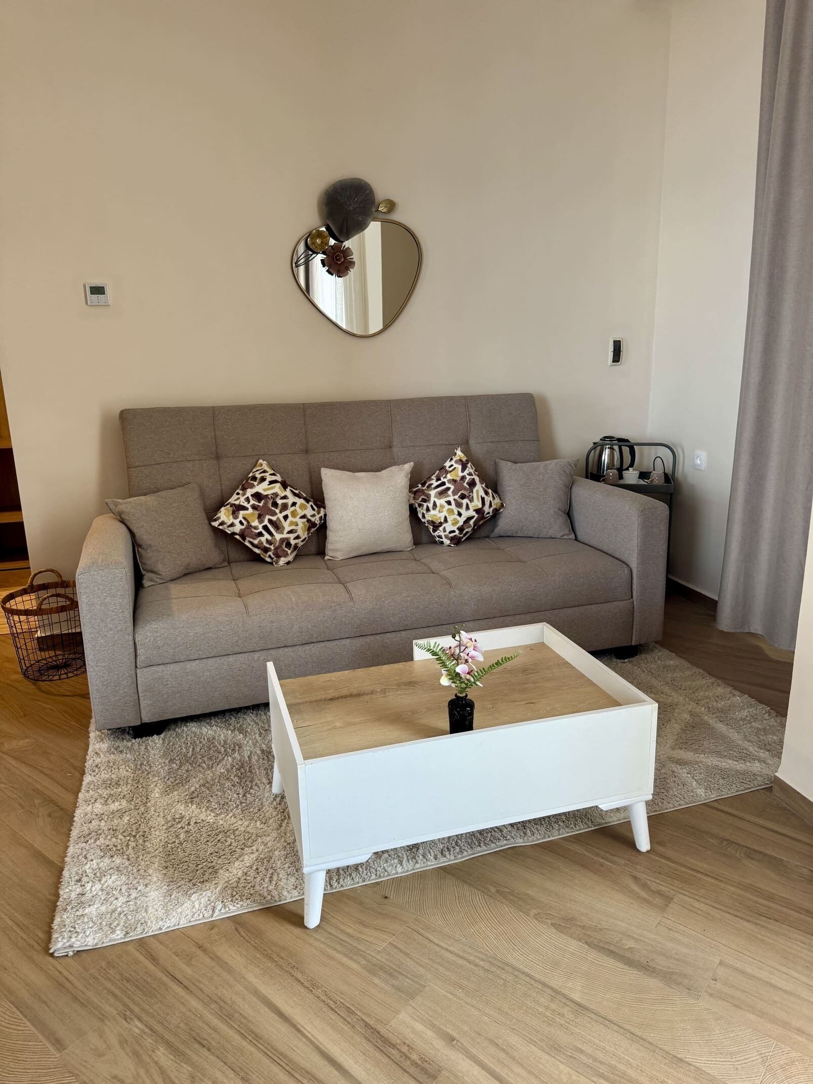Una sala de estar con un sofá gris, una mesa de centro blanca y un espejo en la pared.