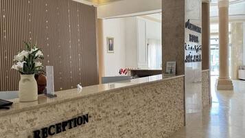 A reception area with a marble counter labeled "RECEPTION," a wooden slat wall, and a large pillar with a sign.