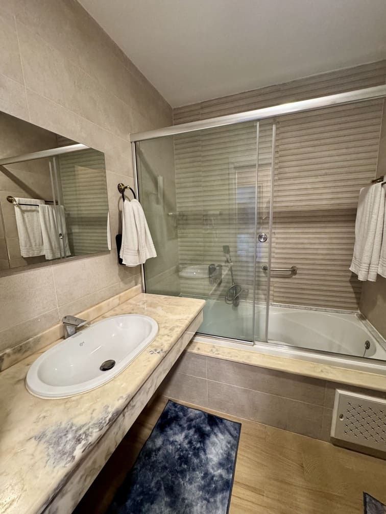 Un baño moderno con ducha envuelta en vidrio, lavamanos de mármol y un espejo grande.