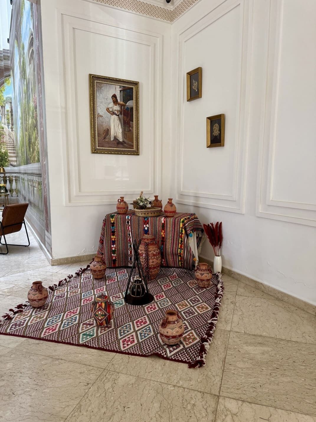 A room with a patterned rug, a table with pottery, and a framed painting on the wall.