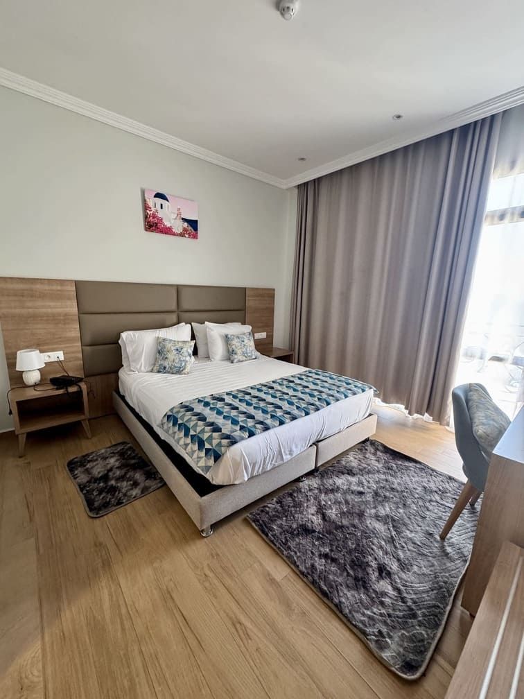 Une chambre d’hôtel moderne, dotée d’un grand lit, d’une table de chevet, d’un bureau et offrant une vue sur l’extérieur.