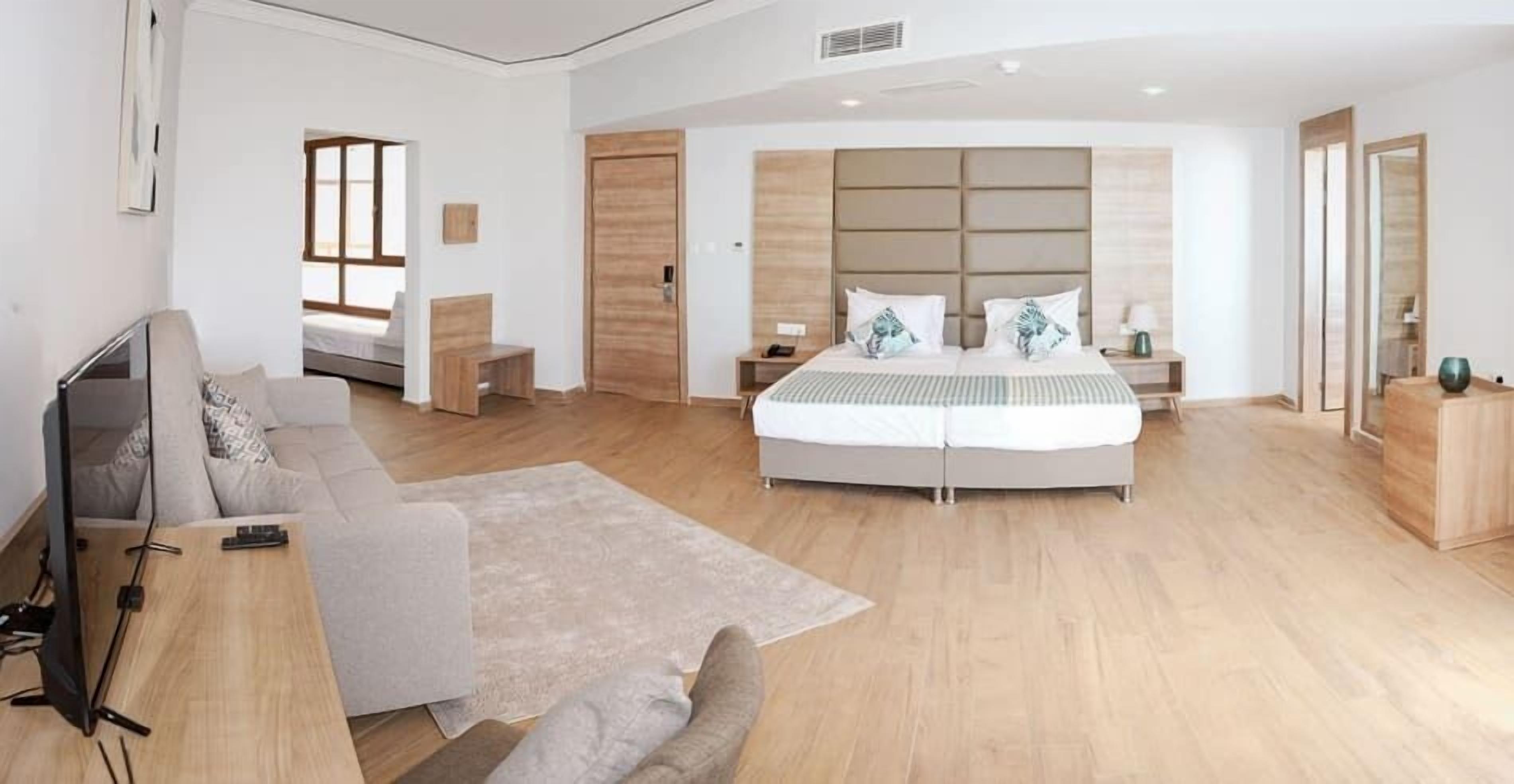 A modern hotel room with a large bed, a sofa, a TV, and a desk.