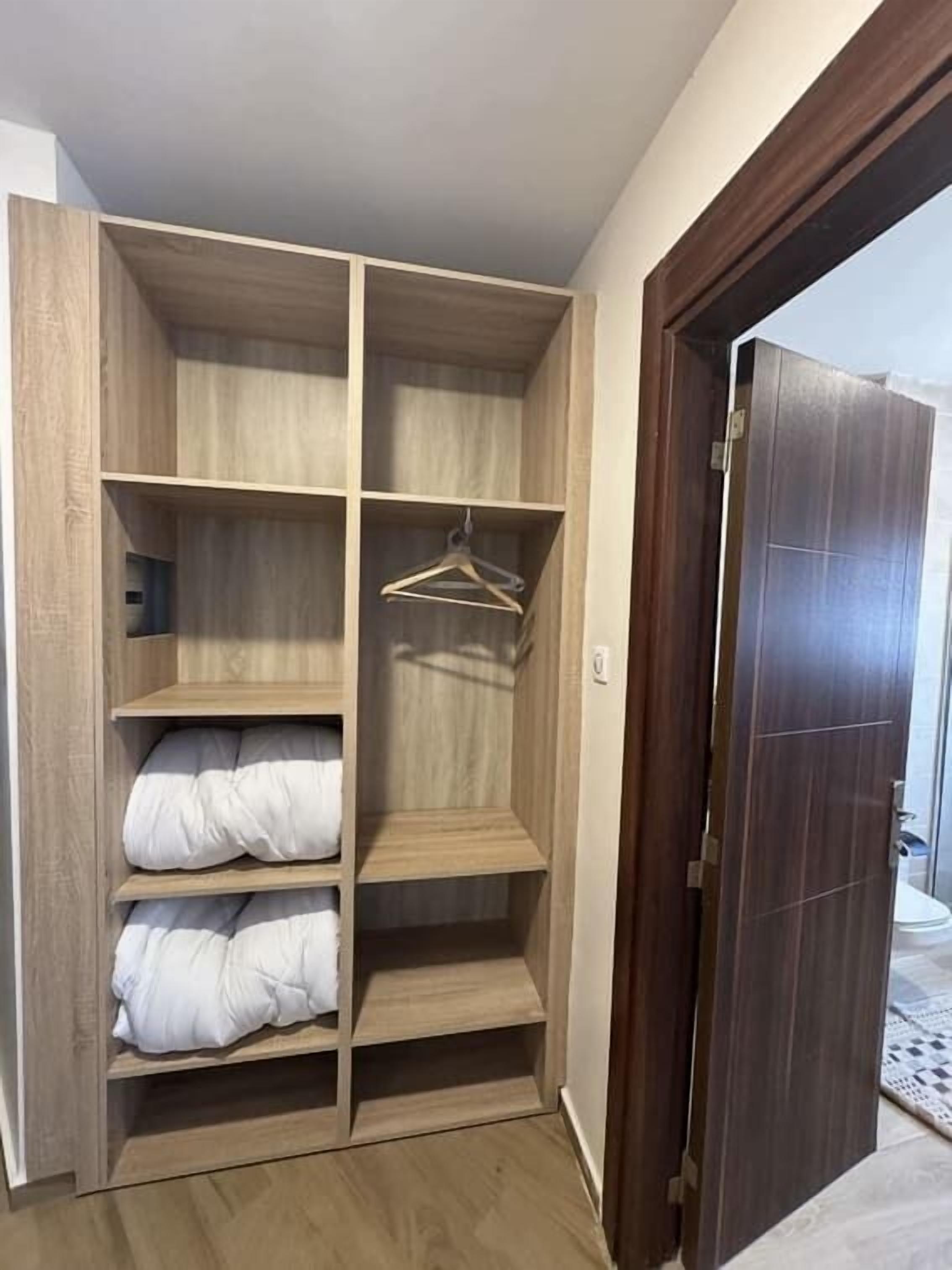Un vestidor con amplias repisas y espacio para colgar, piso de madera y una puerta de madera oscura.