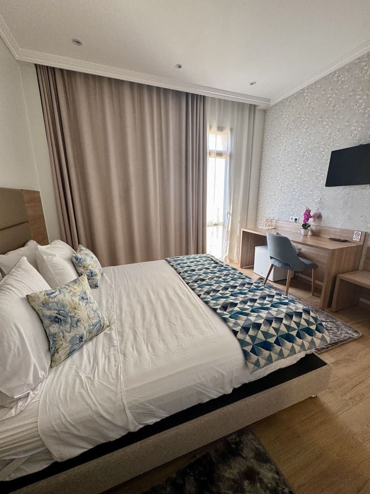 A hotel room with a large bed, a desk, a chair, and a TV mounted on the wall.