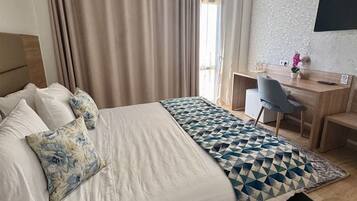 A hotel room with a large bed, a desk, a chair, and a TV mounted on the wall.