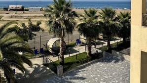 Een balkon met uitzicht op een strand, palmbomen en een heldere lucht.